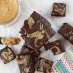 overhead, close up photo of chocolate peanut butter brownies on a wood cutting board with peanut butter in a glass bowl in the background