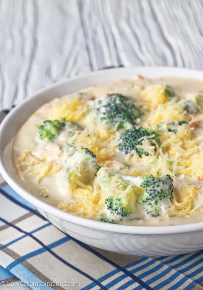 cheesy broccoli and vegetable soup in a white bowl with a golden spoon on a napkin, view from above, close-up